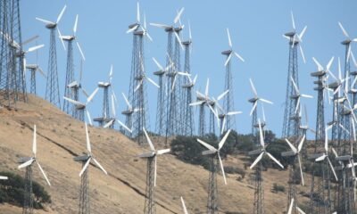 Wind turbines operating across a dry, hilly landscape under a clear blue sky.