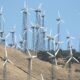 Wind turbines operating across a dry, hilly landscape under a clear blue sky.