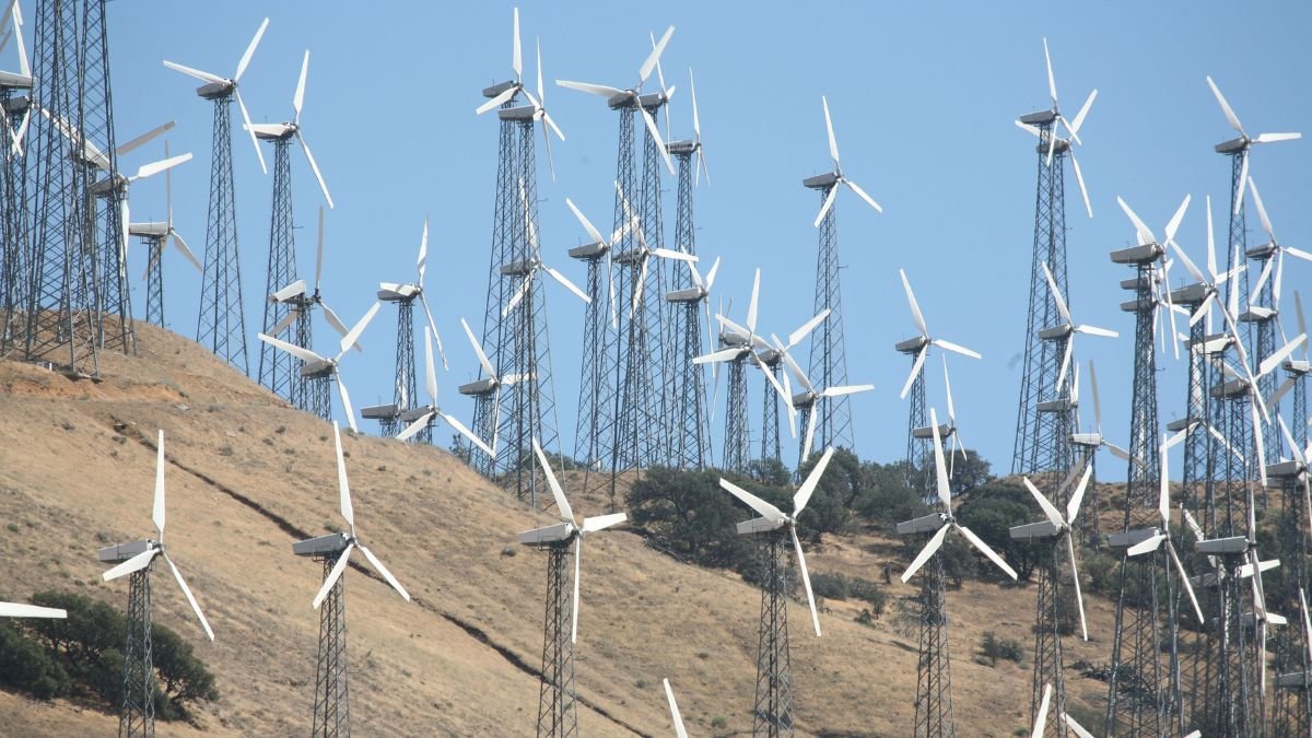 Wind turbines operating across a dry, hilly landscape under a clear blue sky.