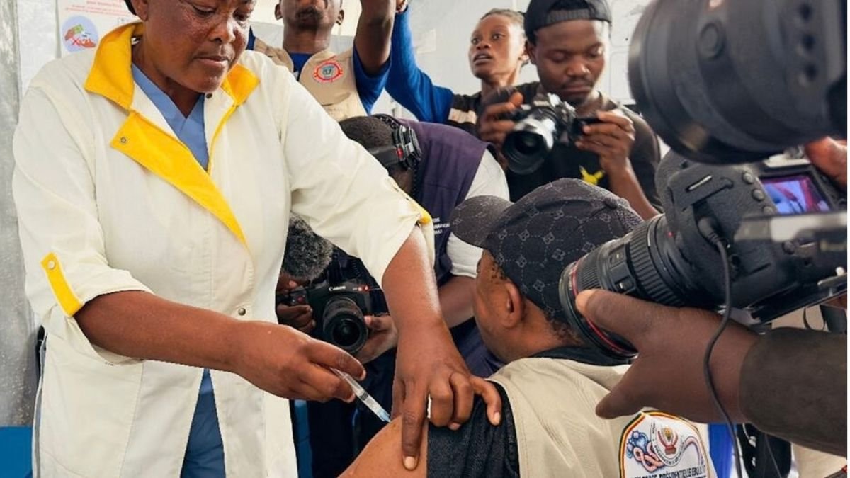 Healthcare worker administers an Ebola vaccine injection to a person as photographers document the vaccination.