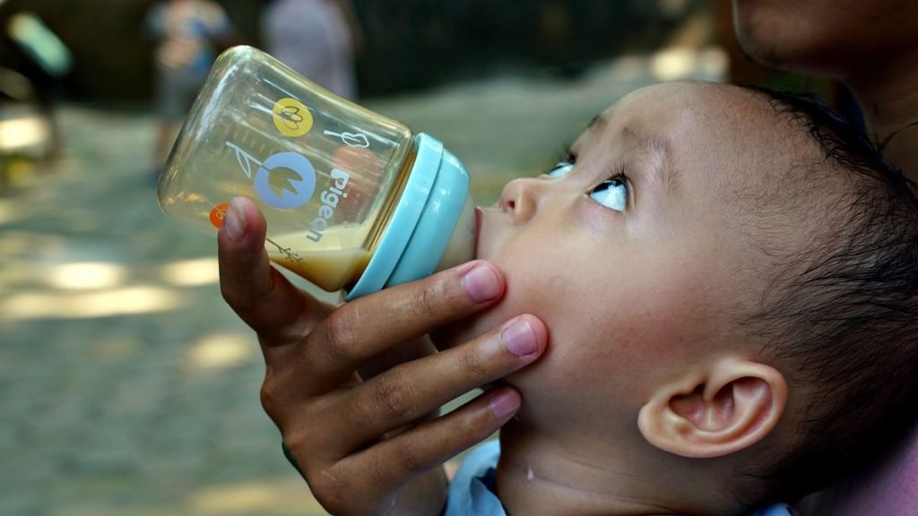 Infant's food: Infant drinking milk from a feeding bottle held by an adult.