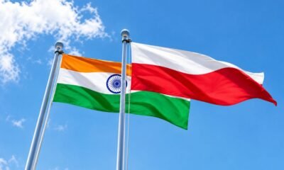 Indian and Polish national flags flying side by side against a blue sky.