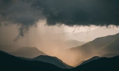 Dark storm clouds and heavy rain over a forested mountain range.