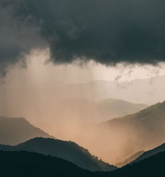Dark storm clouds and heavy rain over a forested mountain range.