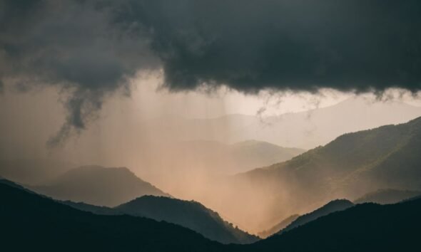 Dark storm clouds and heavy rain over a forested mountain range.
