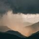 Dark storm clouds and heavy rain over a forested mountain range.