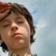 Child shielding his eyes from bright sunlight on a hot day.
