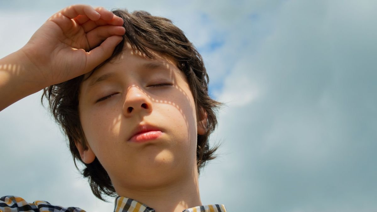 Child shielding his eyes from bright sunlight on a hot day.