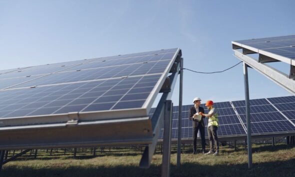 Engineers inspecting solar panels at a solar power installation under a clear blue sky.