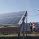 Engineers inspecting solar panels at a solar power installation under a clear blue sky.