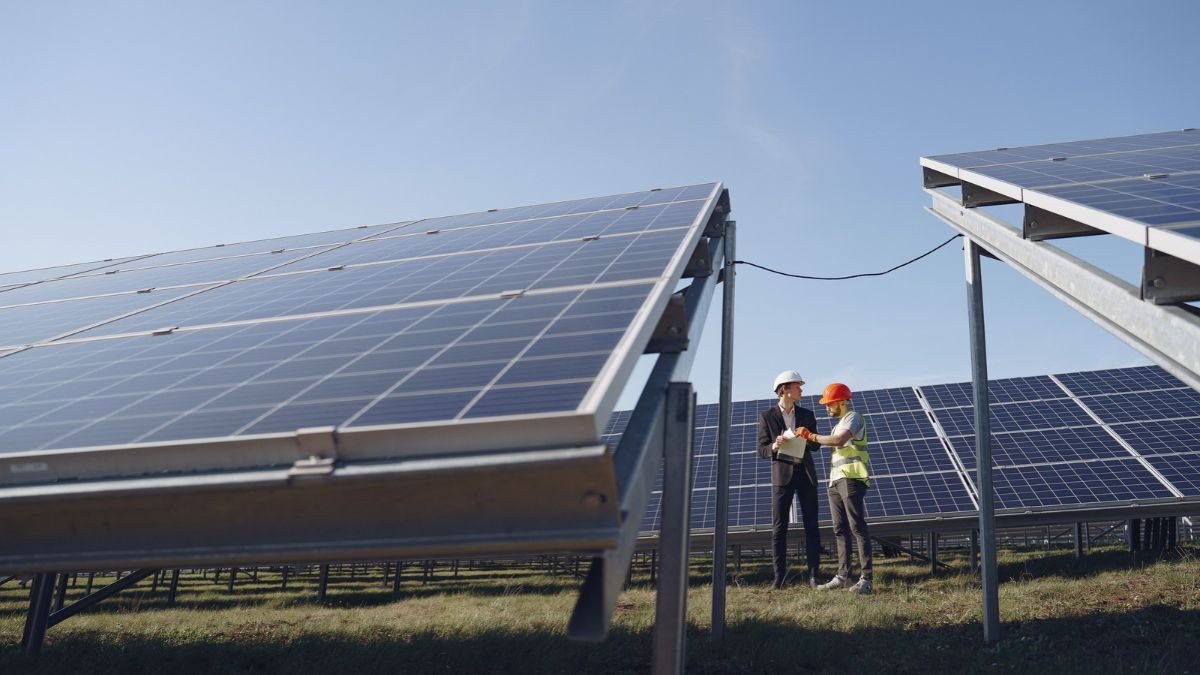 Engineers inspecting solar panels at a solar power installation under a clear blue sky.