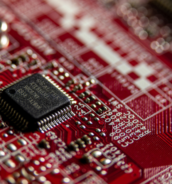 Close-up of a microchip mounted on a red printed circuit board with electronic components and conductive traces.