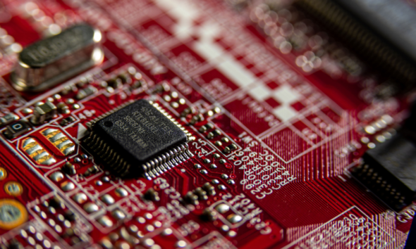 Close-up of a microchip mounted on a red printed circuit board with electronic components and conductive traces.