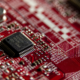 Close-up of a microchip mounted on a red printed circuit board with electronic components and conductive traces.
