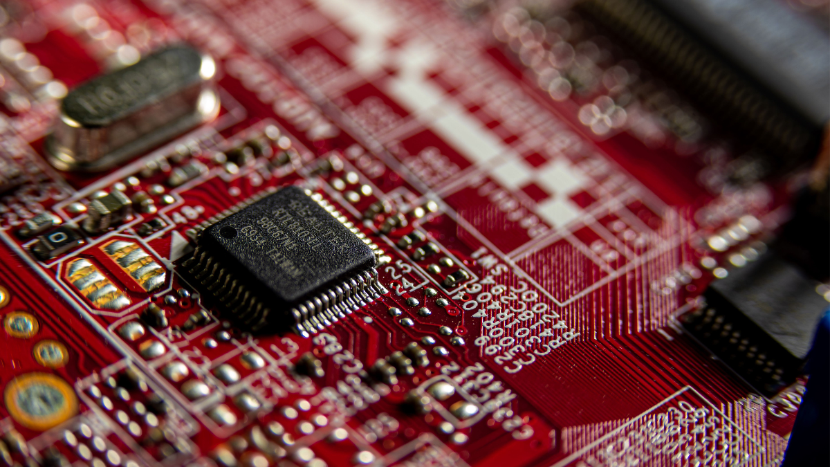 Close-up of a microchip mounted on a red printed circuit board with electronic components and conductive traces.
