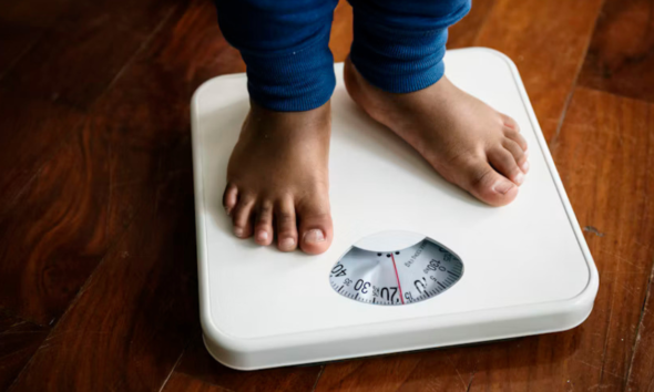 Child standing barefoot on a weighing scale, illustrating childhood obesity and weight monitoring.