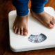 Child standing barefoot on a weighing scale, illustrating childhood obesity and weight monitoring.