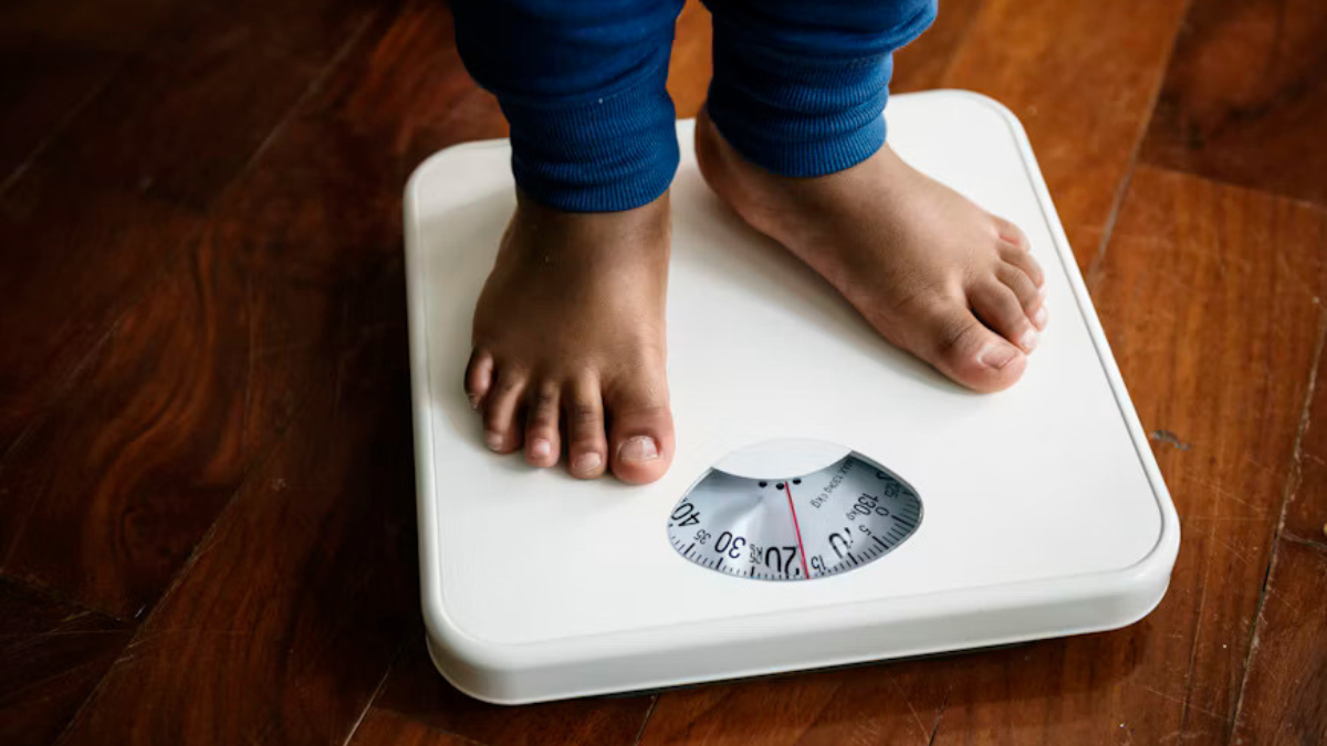 Child standing barefoot on a weighing scale, illustrating childhood obesity and weight monitoring.