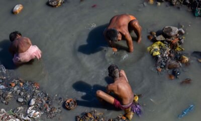 Manual scavenging: Three sanitation workers manually clean a garbage-filled, polluted waterway while standing and crouching in contaminated water, illustrating the hazardous conditions faced by workers involved in manual scavenging and sanitation work.