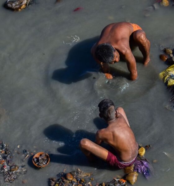 Manual scavenging: Three sanitation workers manually clean a garbage-filled, polluted waterway while standing and crouching in contaminated water, illustrating the hazardous conditions faced by workers involved in manual scavenging and sanitation work.