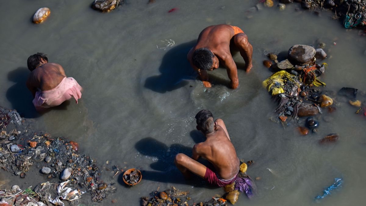 Manual scavenging: Three sanitation workers manually clean a garbage-filled, polluted waterway while standing and crouching in contaminated water, illustrating the hazardous conditions faced by workers involved in manual scavenging and sanitation work.