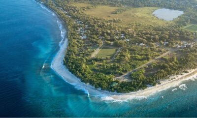 Aerial view of a coastal community in the Marshall Islands, with turquoise waters, sandy beaches, homes, roads and green vegetation along the shoreline.