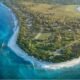 Aerial view of a coastal community in the Marshall Islands, with turquoise waters, sandy beaches, homes, roads and green vegetation along the shoreline.