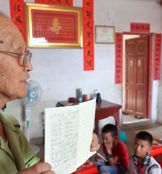 Teacher workforce: An older teacher holds a lesson book while teaching a group of children in a classroom.