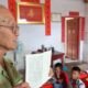 Teacher workforce: An older teacher holds a lesson book while teaching a group of children in a classroom.
