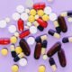 Cancer medicine price regulation in India illustrated by assorted tablets and capsules on a purple background.