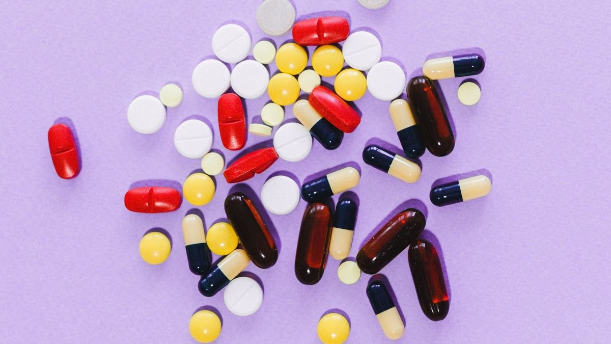 Cancer medicine price regulation in India illustrated by assorted tablets and capsules on a purple background.