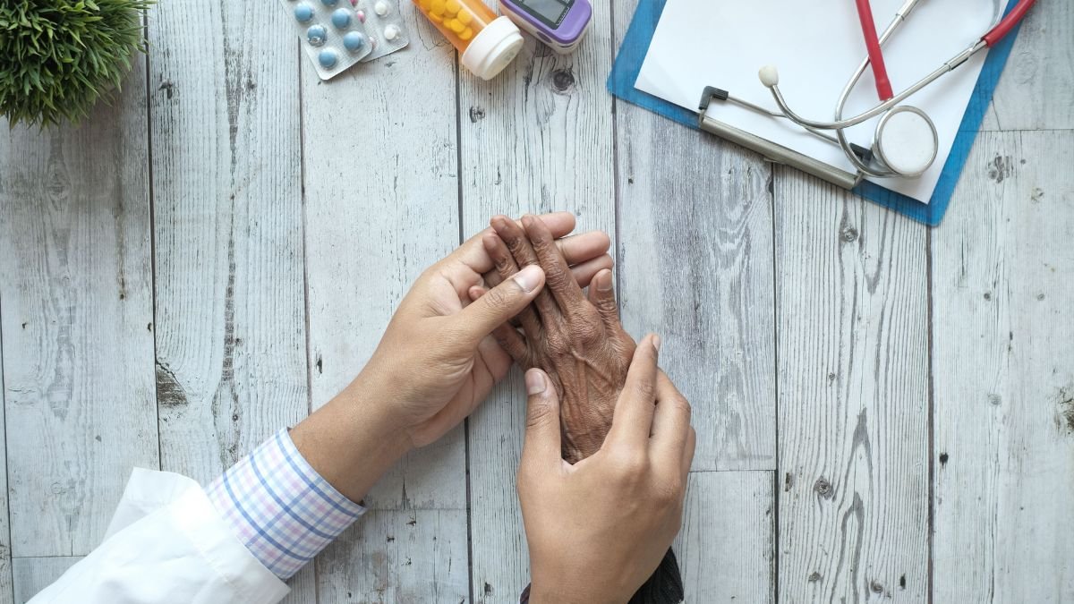 Healthcare professional holding an older adult’s hand during a medical consultation, illustrating research into healthy ageing and age-related health risks.
