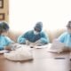 NMC: Medical professionals in protective equipment review documents during a patient safety meeting.
