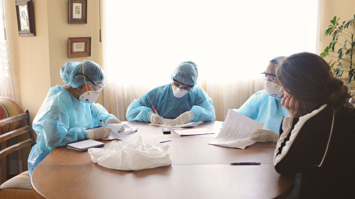NMC: Medical professionals in protective equipment review documents during a patient safety meeting.