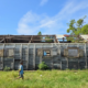A child walks past a weather-damaged wooden school building with a partially missing roof.
