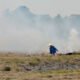 A farmer burns crop residue in a harvested agricultural field as thick smoke rises into the air.