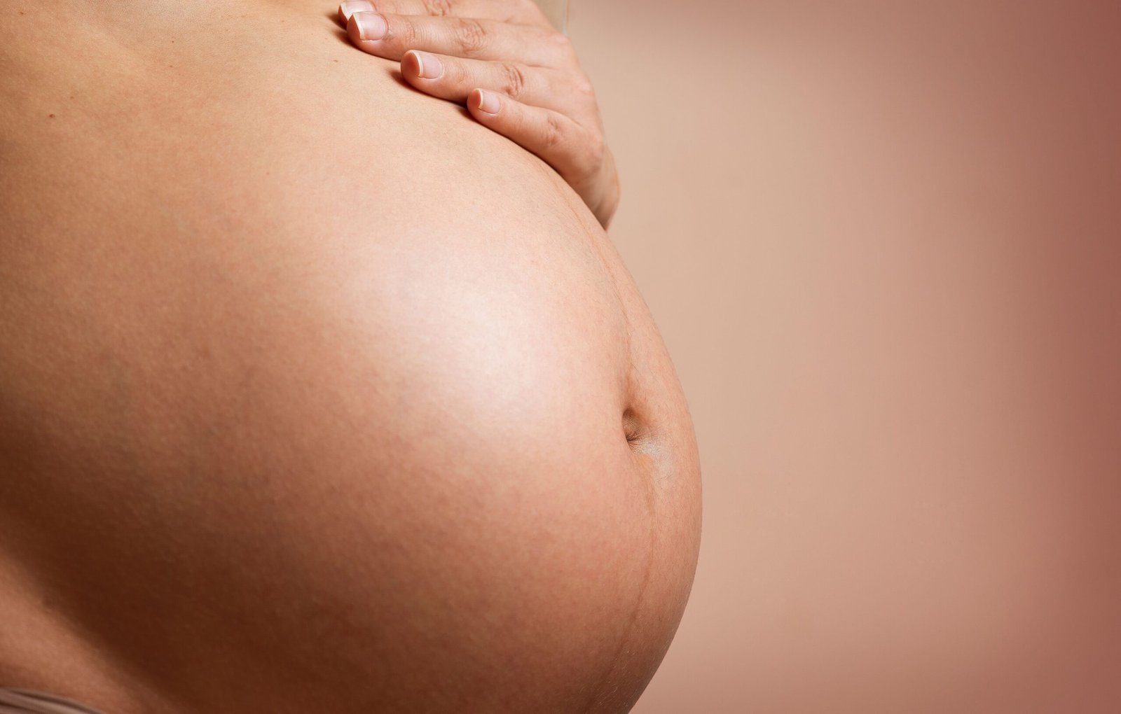 Close-up of a pregnant woman gently resting her hand on her abdomen.