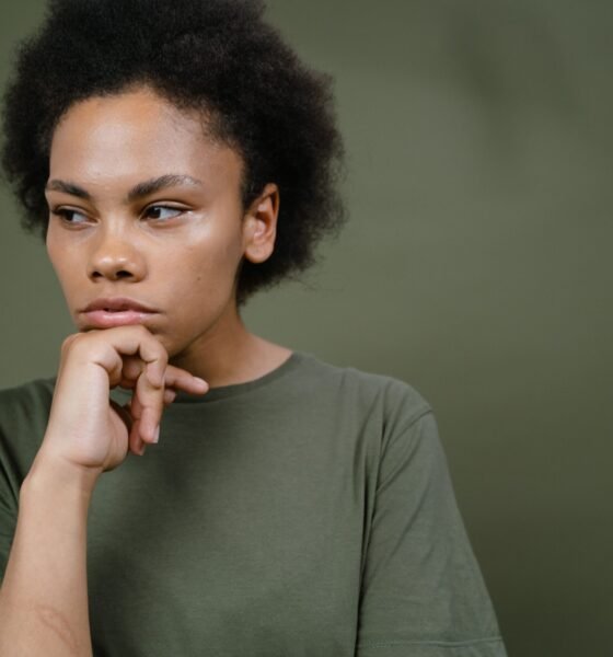 A young woman with natural curly hair resting her chin on her hand and looking thoughtfully to the side.