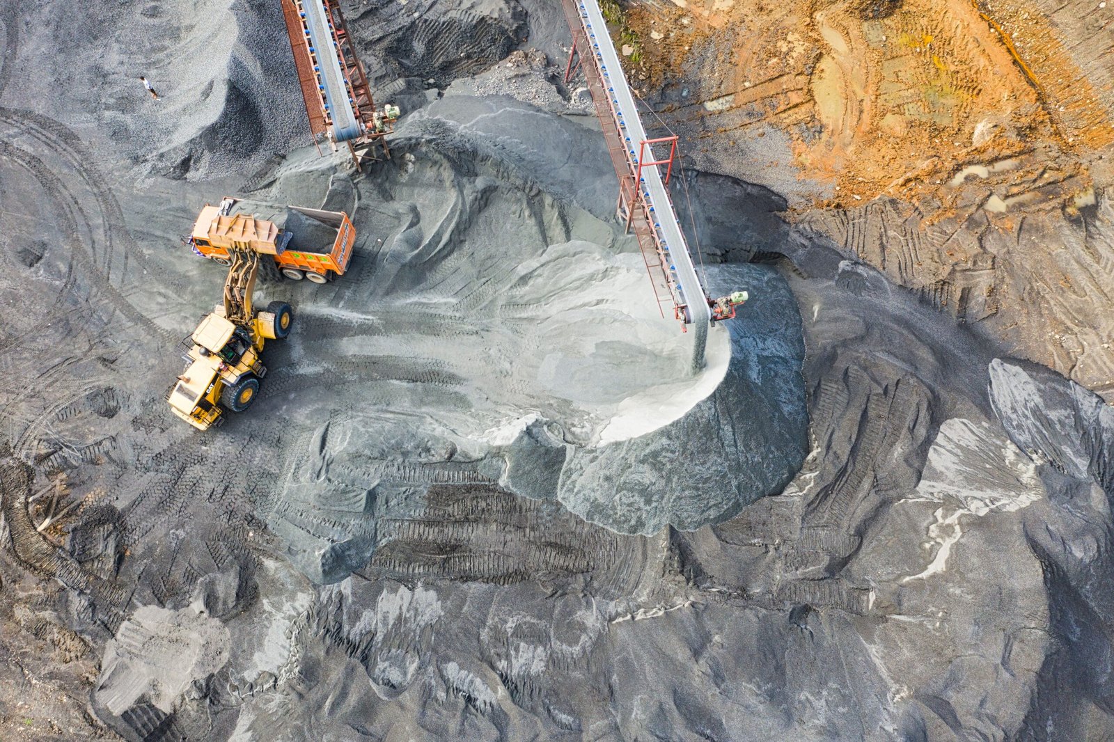 Open-pit coal mine with heavy machinery, conveyor belts and piles of extracted coal.